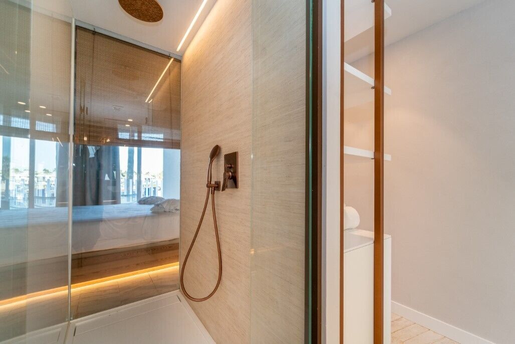 A modern bathroom with a glass shower enclosure, a wooden floor, and a view of the city through the glass.