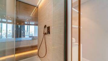 A modern bathroom with a glass shower enclosure, a wooden floor, and a view of the city through the glass.
