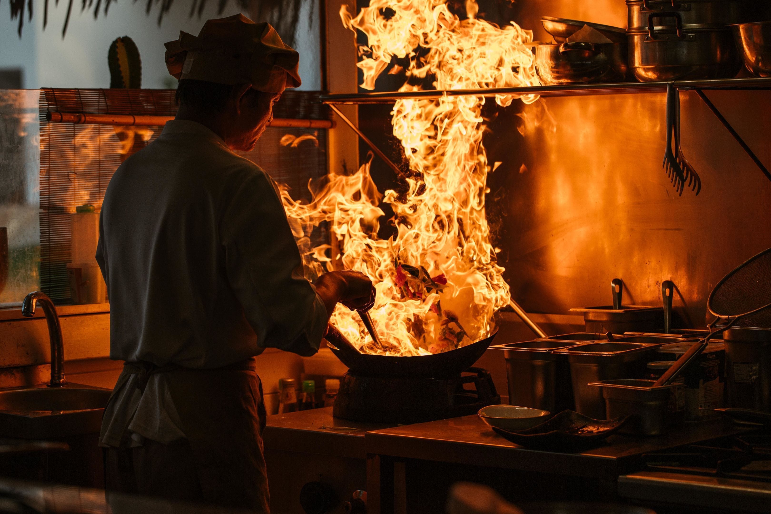 Un chef cuisinant dans un grand wok sur une cuisinière, entouré d’ustensiles de cuisine et de différents types de casseroles.