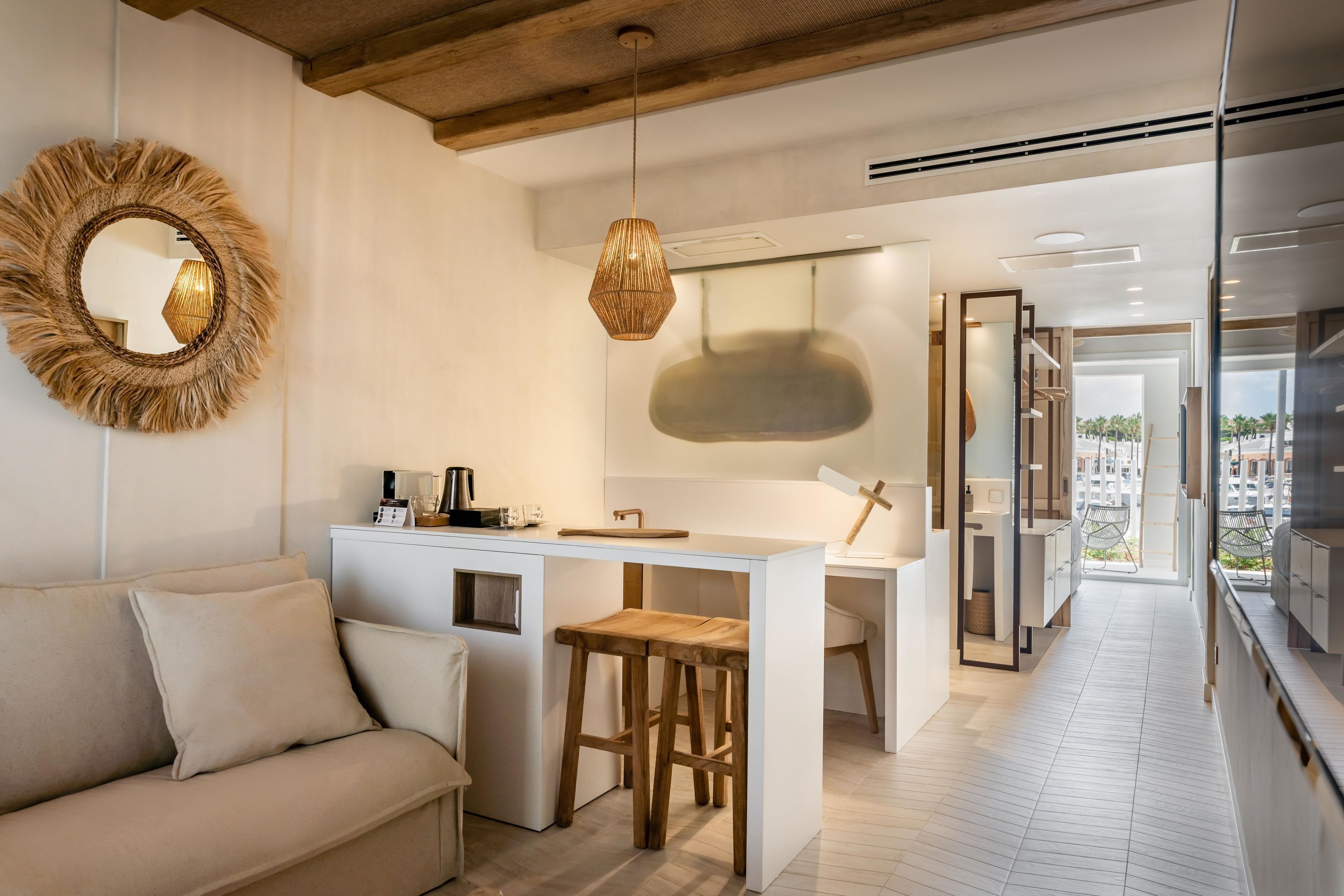 A modern kitchen with a central island, wooden stools, and a hanging light fixture.