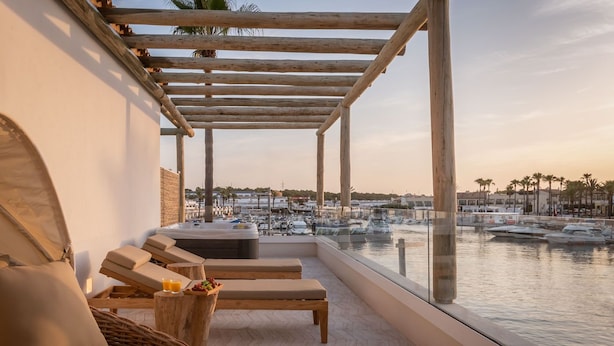 A balcony with wooden furniture, a hot tub, and a view of a marina. - Lago Resort Menorca Suites del Lago - Adults Only (Ciutadella de Menorca)