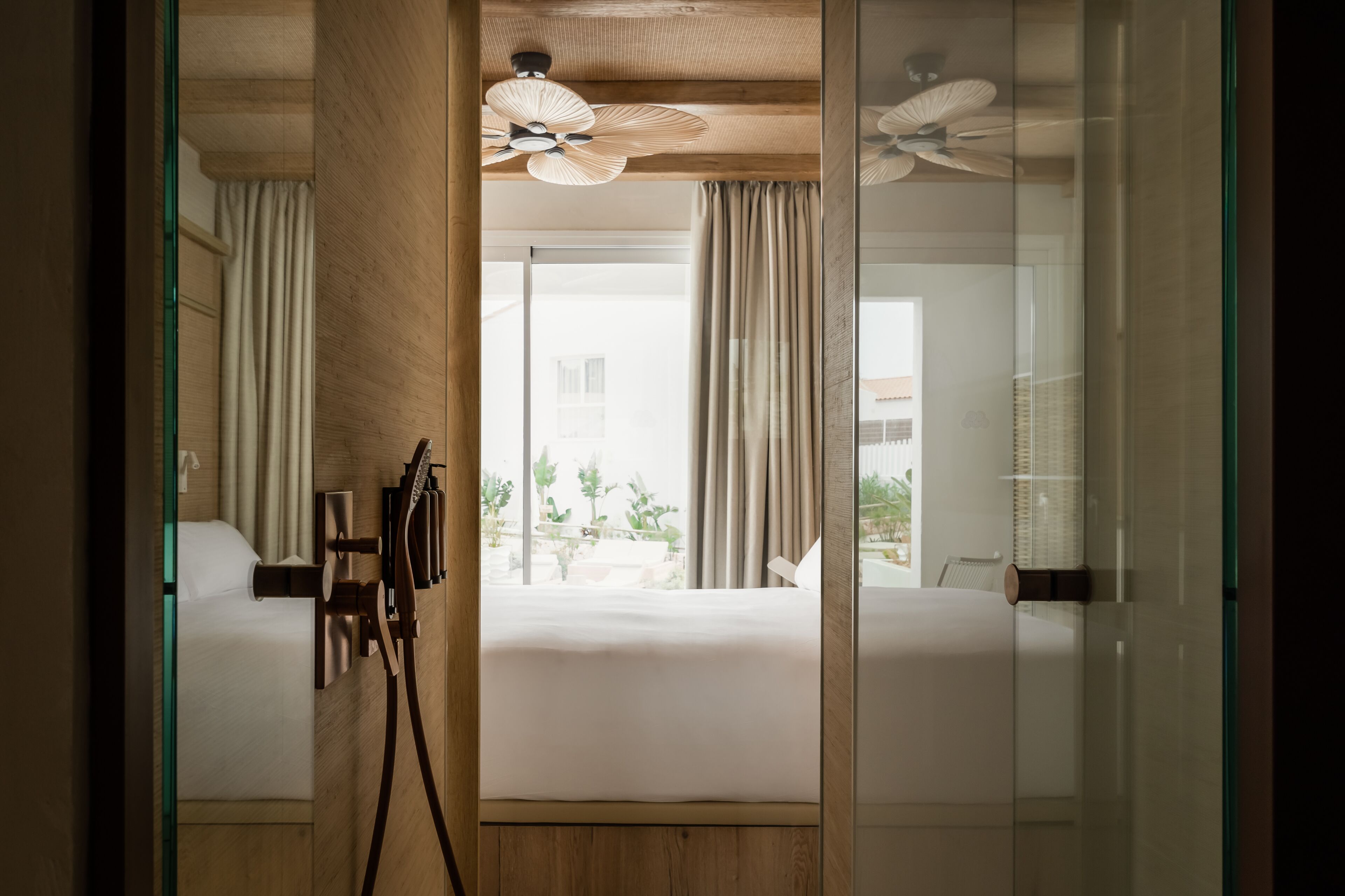 A modern hotel room with a large bed, a ceiling fan, and a view of the outdoors.
