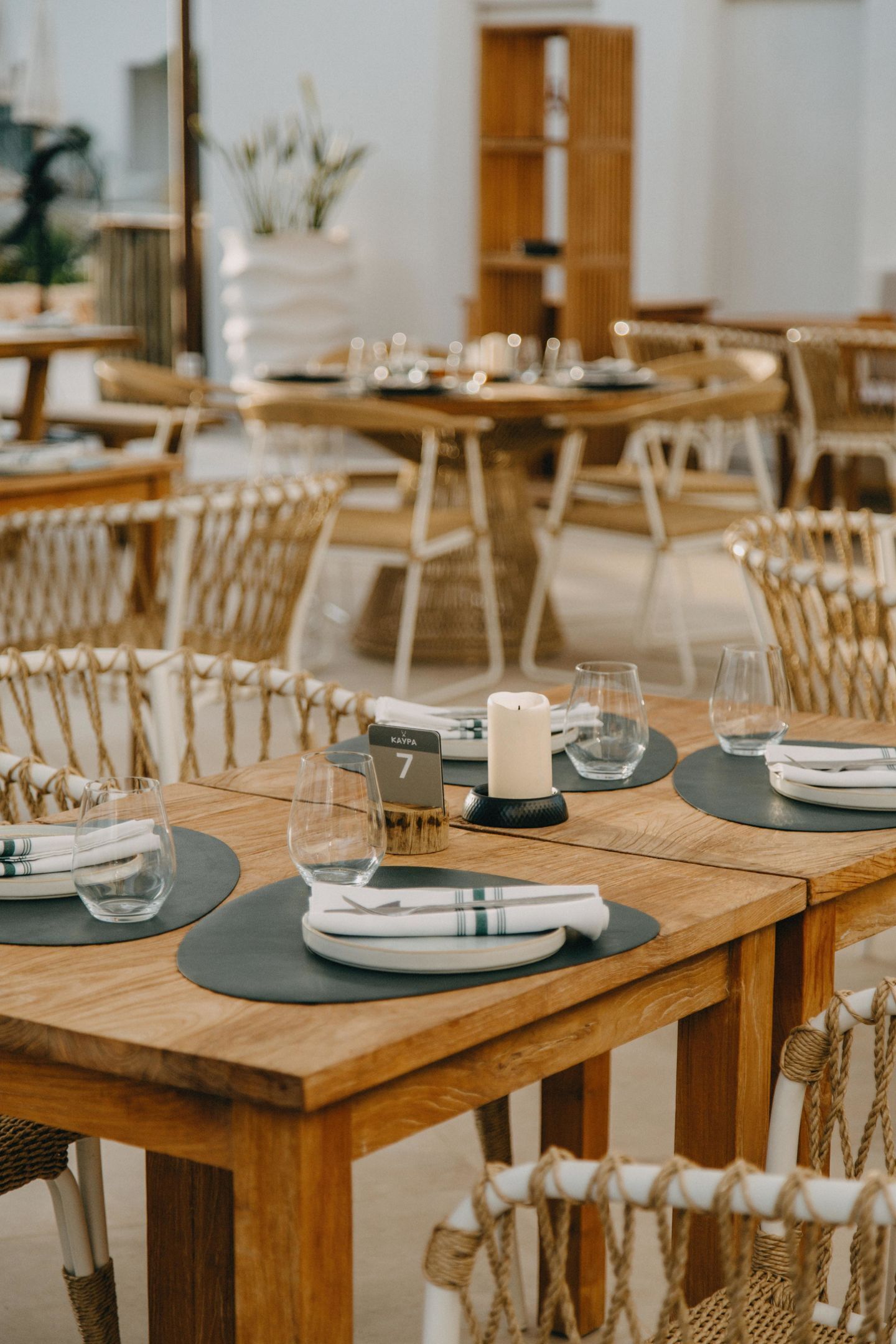 Un espace repas avec des tables en bois et des chaises en osier, chaque table étant dressée avec des assiettes, des couverts et des verres.