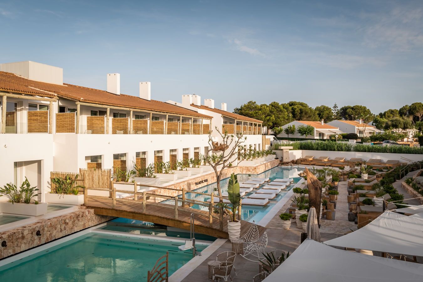 Zona de piscina con sillones de descanso y un edificio con varios balcones.