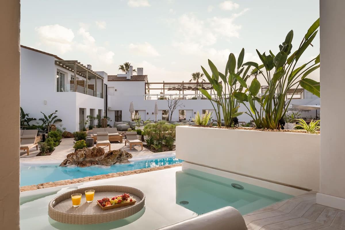 A pool area with a dining setup, lounge chairs, and tropical plants.