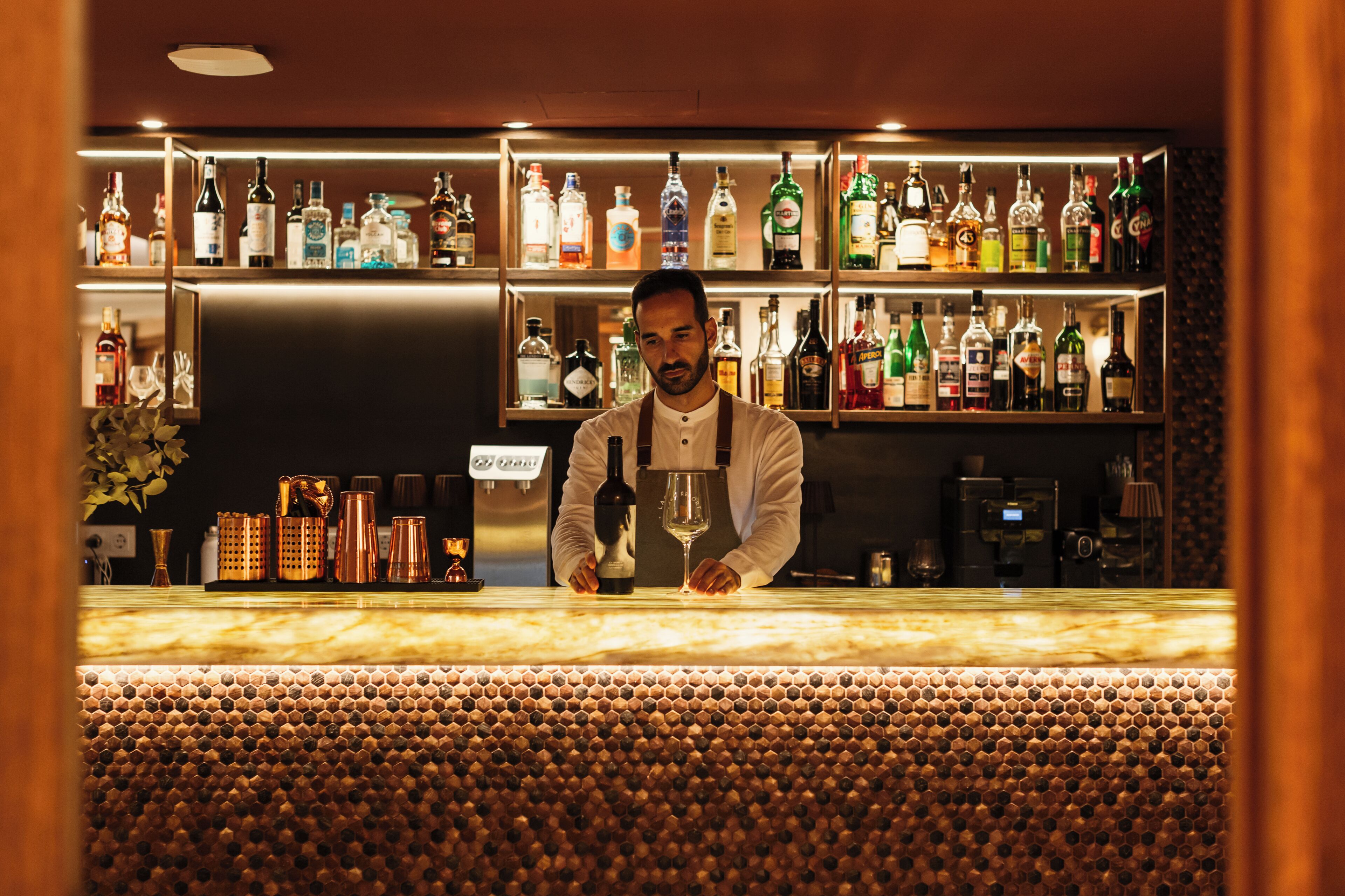 A bar area with shelves of various liquor bottles, a bar counter, and a coffee machine.