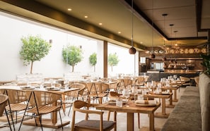 A restaurant with wooden tables and chairs, large windows, and a bar area.