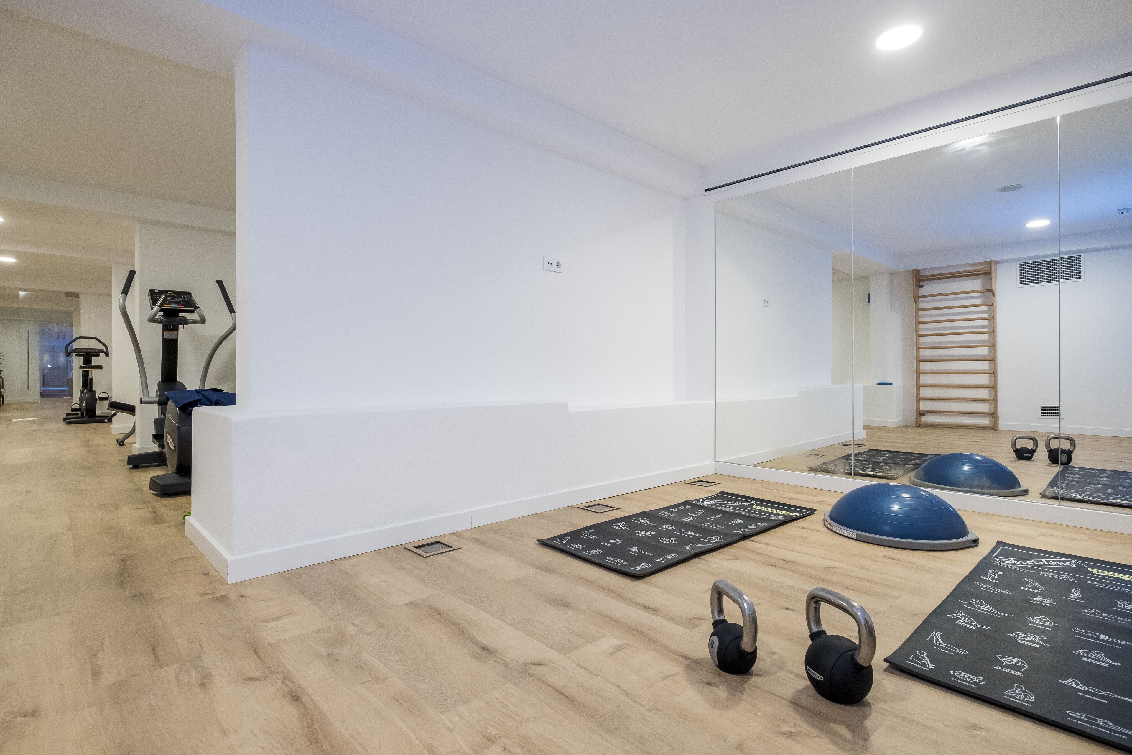 Une salle de sport moderne équipée de matériel d’exercice, dotée d’un mur miroir et d’un plancher en bois.