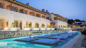 A modern hotel with a pool area featuring lounge chairs and a stone wall. - Lago Resort Menorca Suites del Lago - Adults Only (Ciutadella de Menorca)