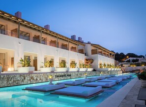A modern hotel with a pool area featuring lounge chairs and a stone wall. - Lago Resort Menorca Suites del Lago - Adults Only (Ciutadella de Menorca)