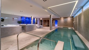A modern indoor swimming pool with clear glass railings, a spa area, and a reception desk. - Lago Resort Menorca Suites del Lago - Adults Only (Ciutadella de Menorca)