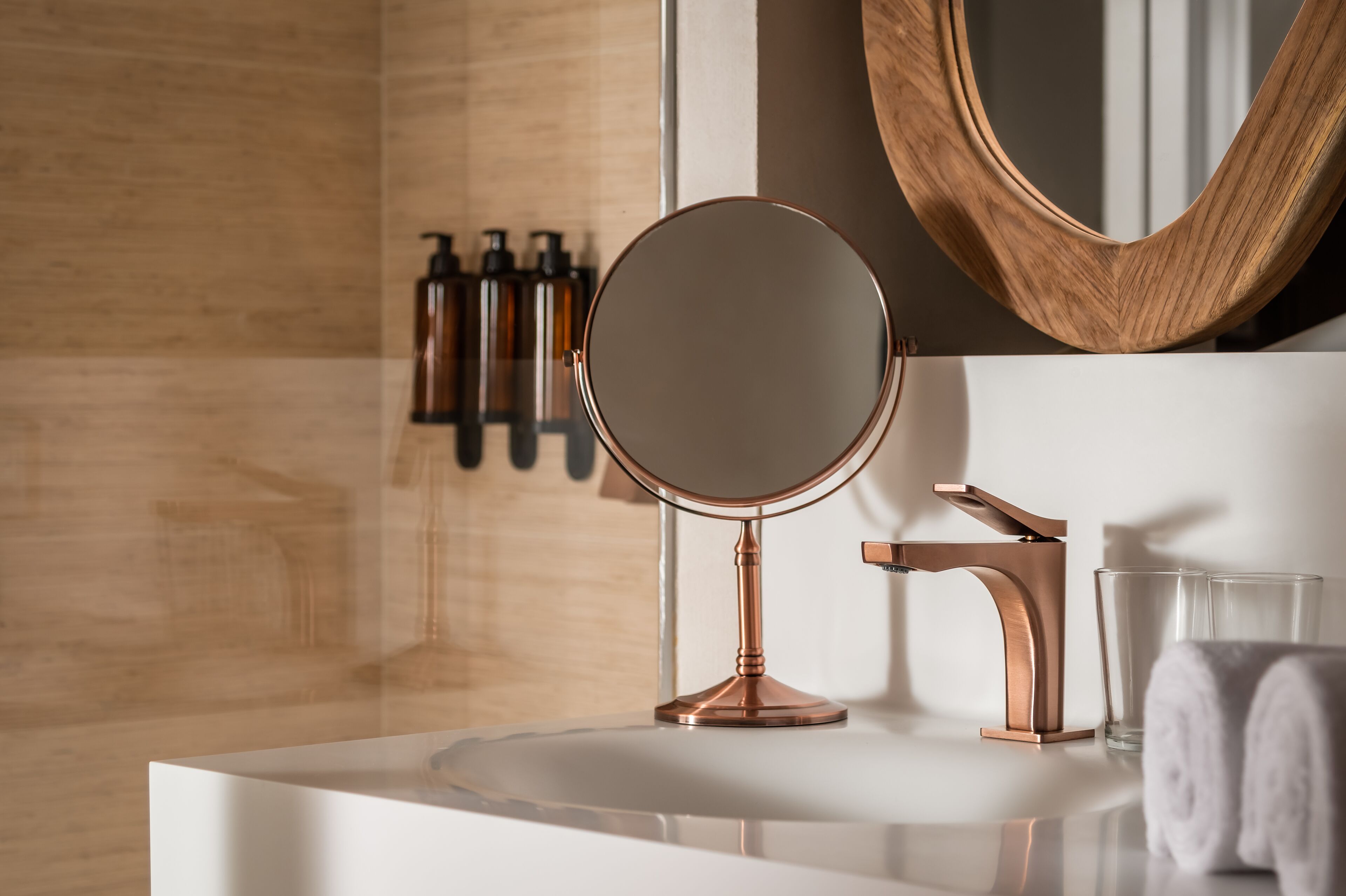 A bathroom with a round mirror, copper faucet, and toiletries on the wall.