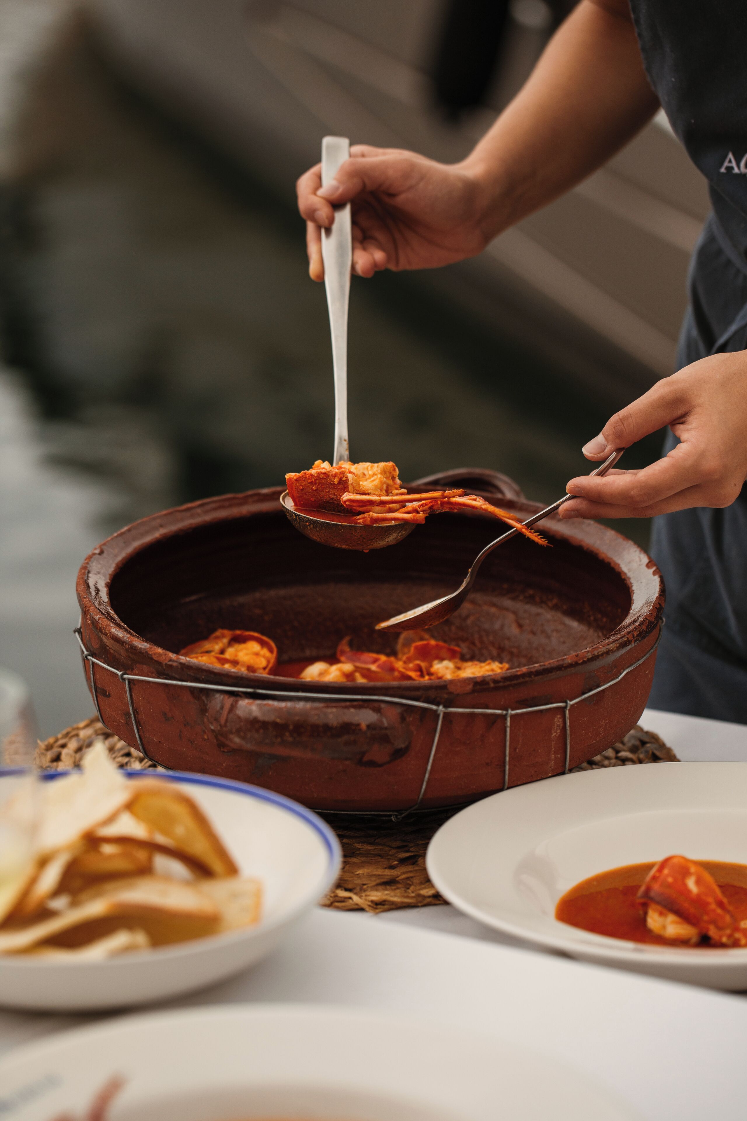 A person serving food from a large, rustic, brown pot.