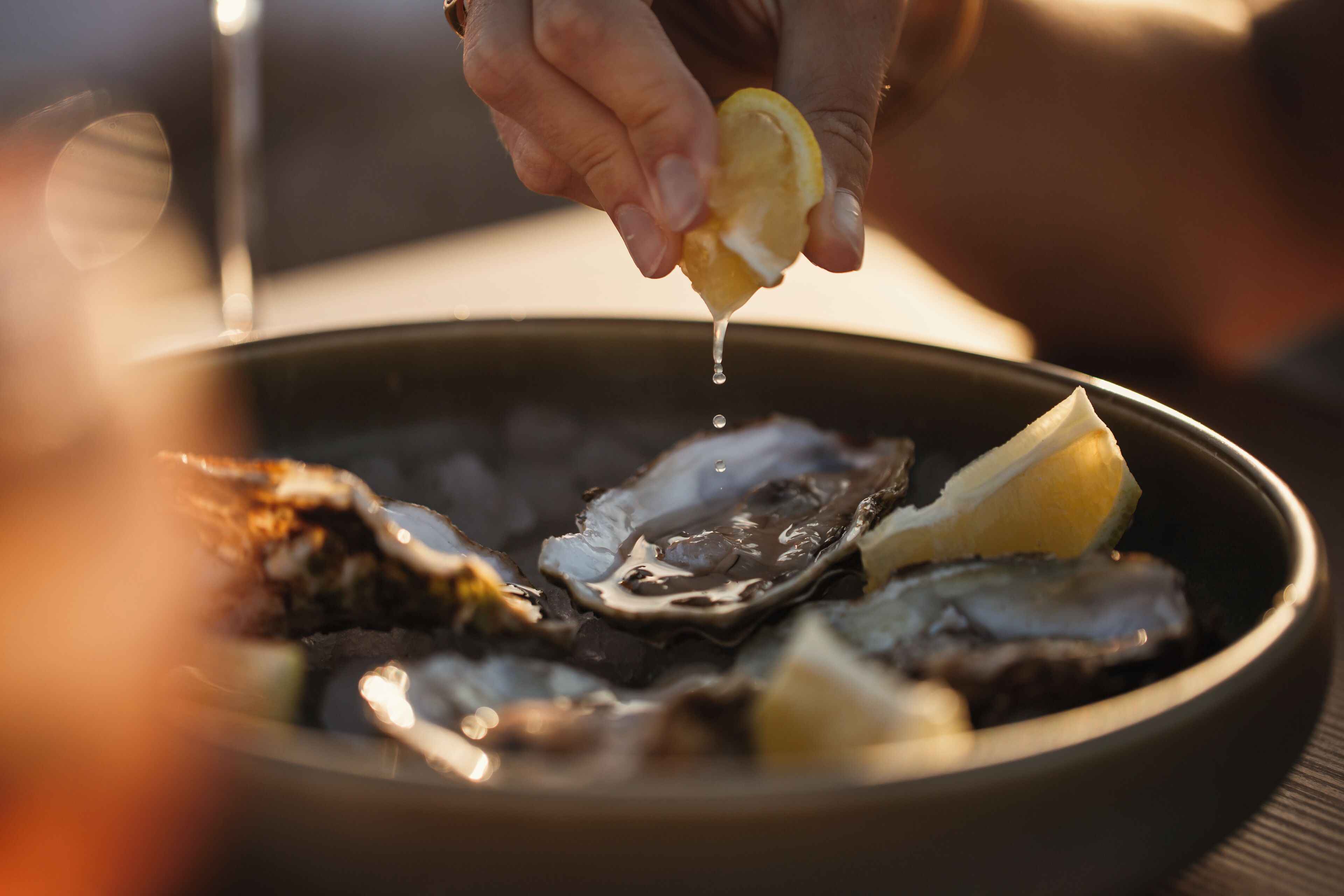 A bowl of oysters with lemon wedges and a hand squeezing lemon juice over them.