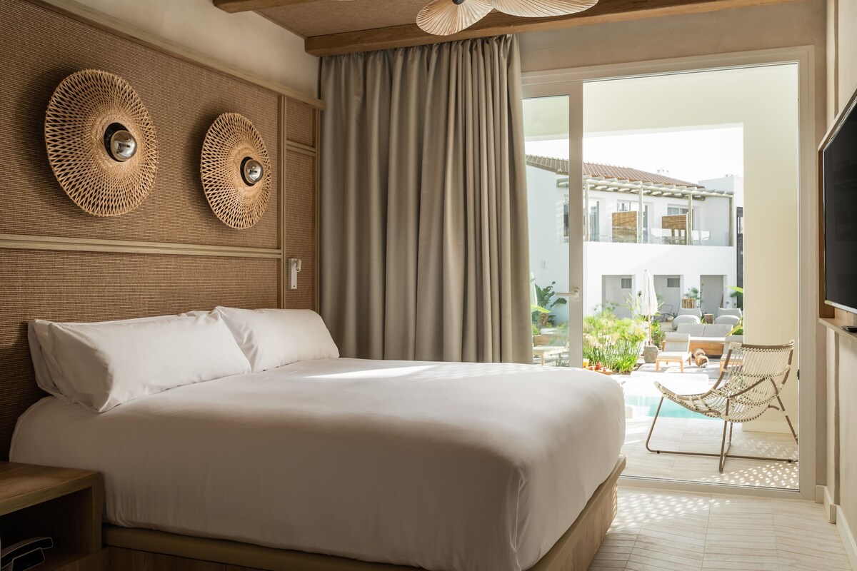 A hotel room with a large bed, a ceiling fan, and a view of the outdoor pool area.