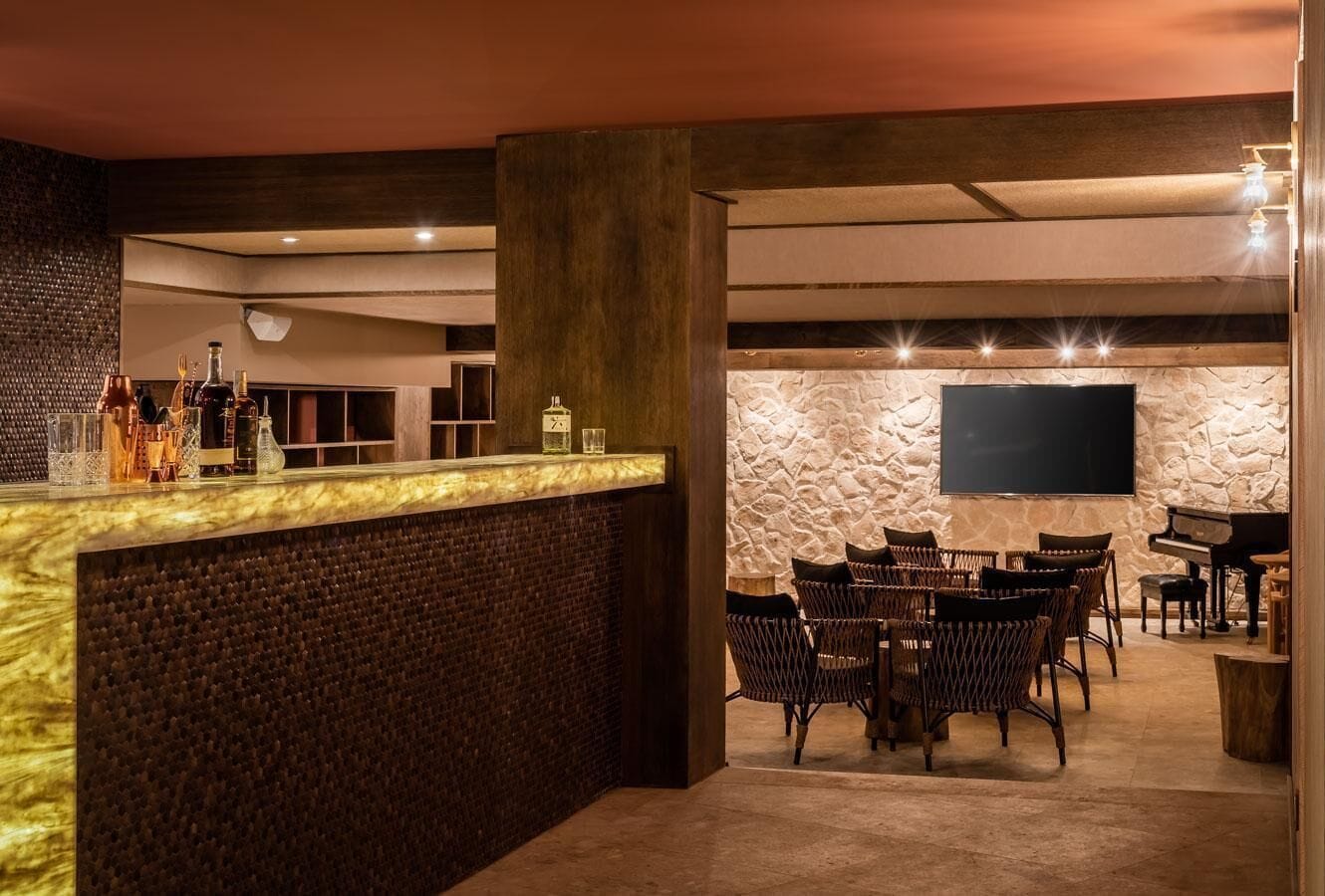 Een bar met een stenen muur, een flatscreen televisie, rieten stoelen en een piano.
