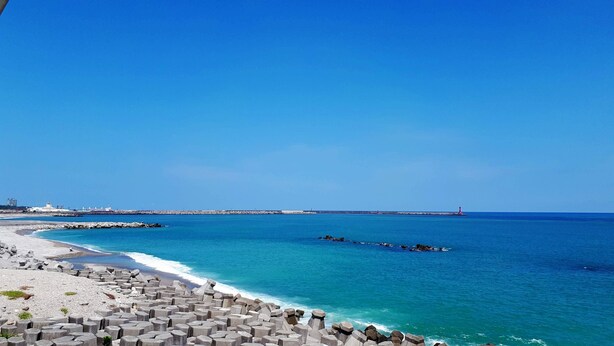 Une vue sur la côte, avec un ciel dégagé, une plage de sable et une digue rocheuse.