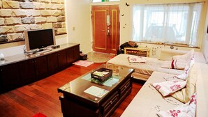Un salon avec un mur en pierre, un téléviseur posé sur un meuble, un canapé et une fenêtre avec des rideaux.