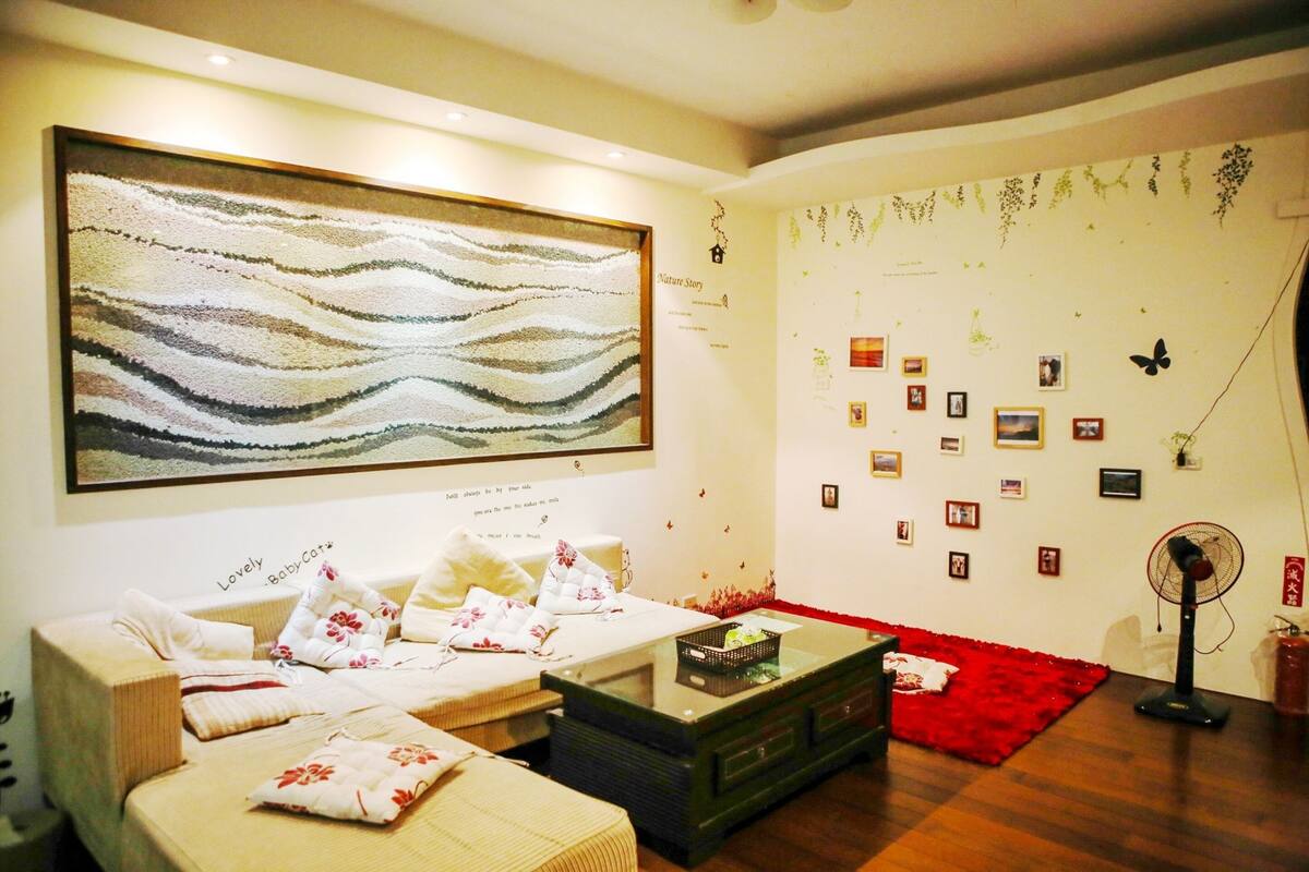 Een gezellige woonkamer met een groot abstract schilderij, een bank, een bijzettafeltje en een rood vloerkleed.