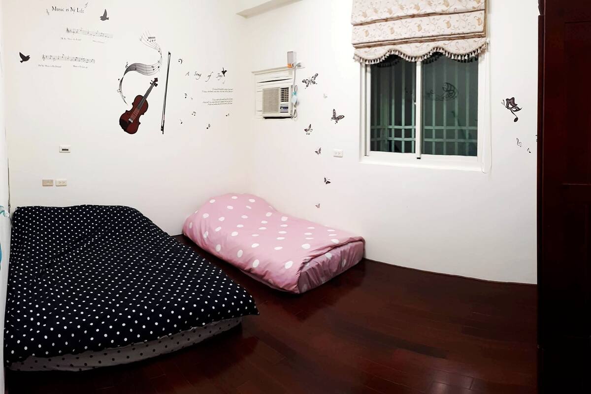 Een kamer met een bed, een raam en wanddecoraties, waaronder een viool en muzieknoten.