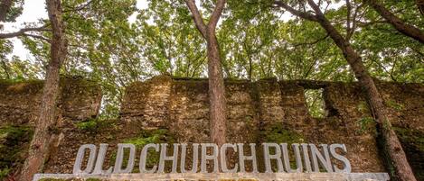 A sign reading "Old Church Ruins" set against a backdrop of trees and stone ruins.