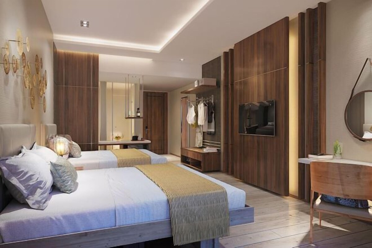 A modern bedroom with two beds, a vanity, a TV, and a mirror.