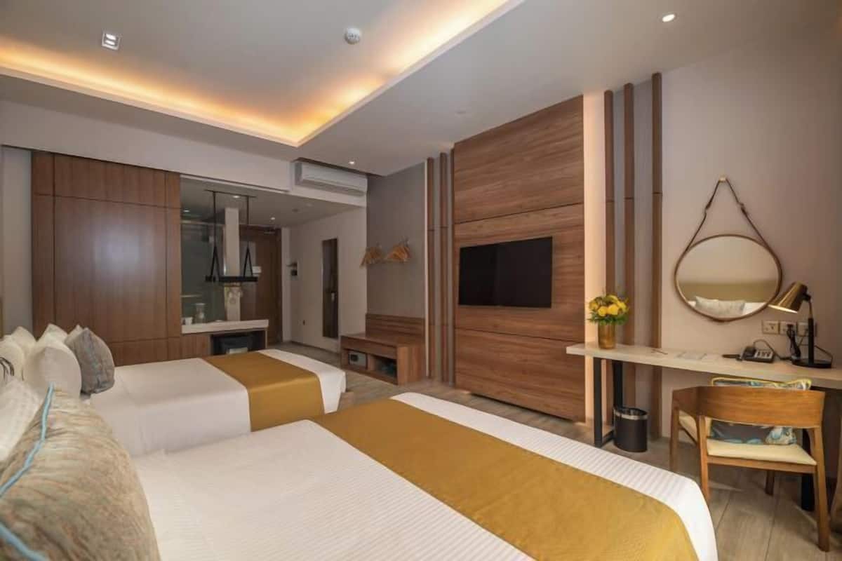 A hotel room with two beds, a TV, a desk, and a mirror.