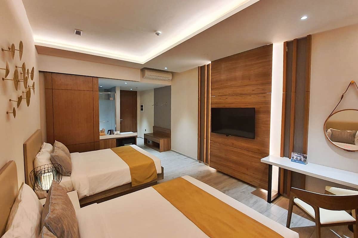 A hotel room with two beds, a TV, a desk, and a mirror.
