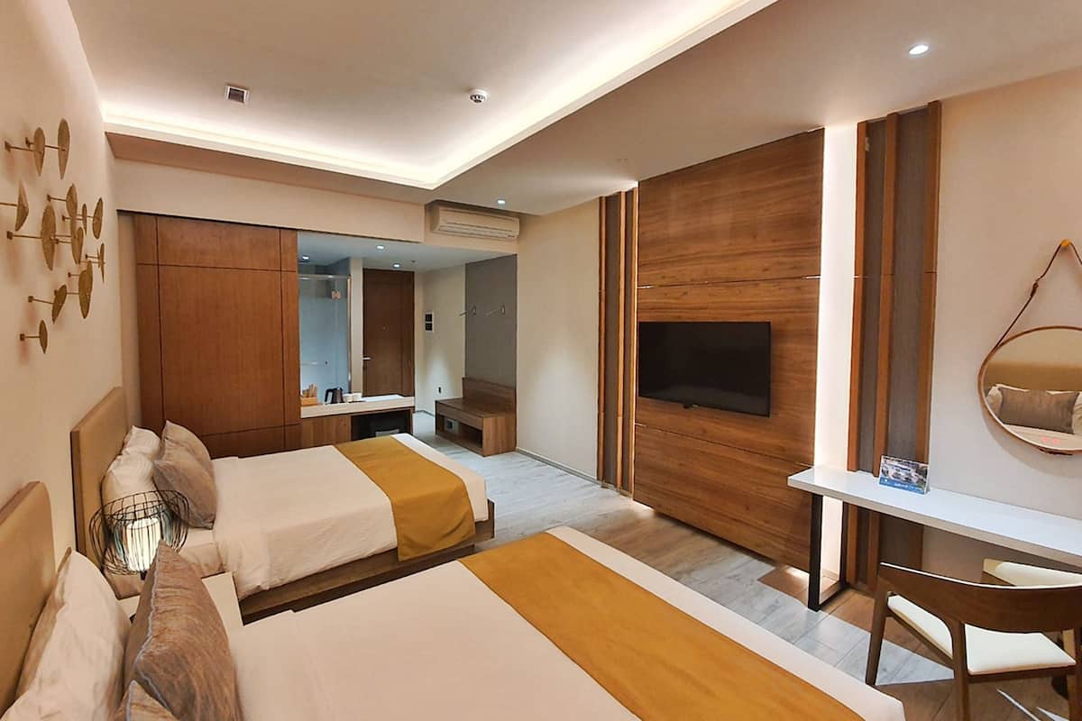 A hotel room with two beds, a TV, a desk, and a mirror.