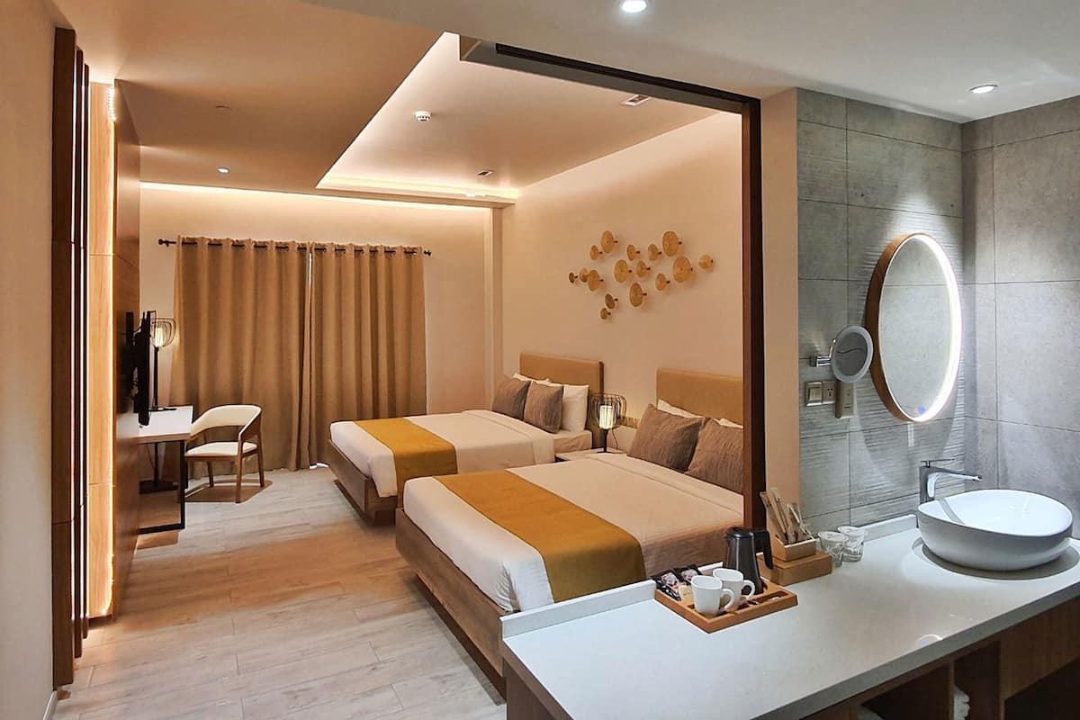 A hotel room with two beds, a desk, a chair, a bathroom with a sink and mirror, and a tray with toiletries.