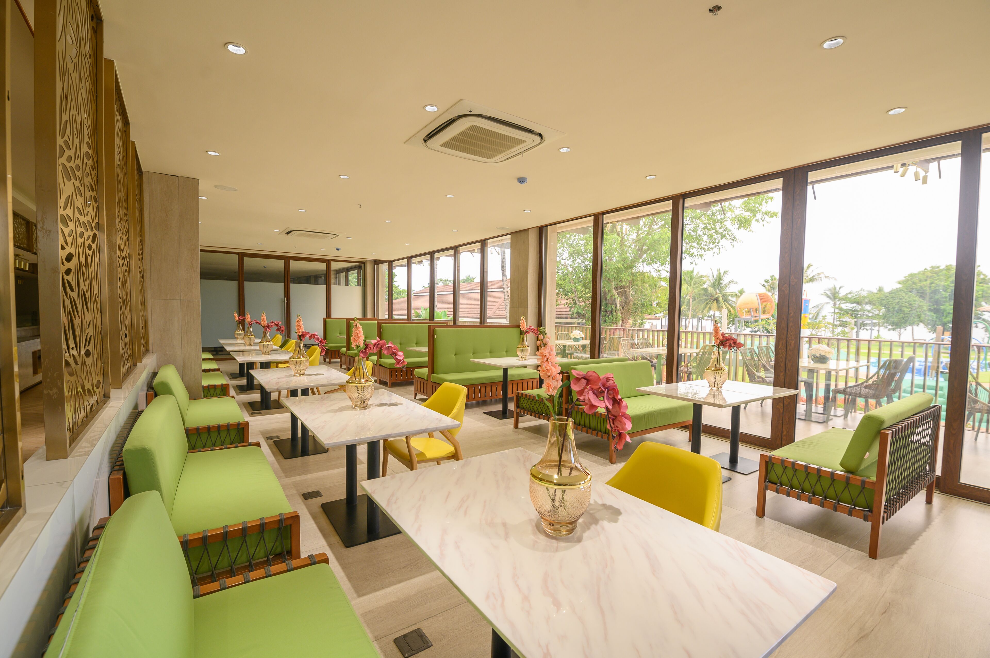 Un restaurante con asientos acolchados de color verde, mesas de mármol y grandes ventanales que ofrecen vistas al exterior.