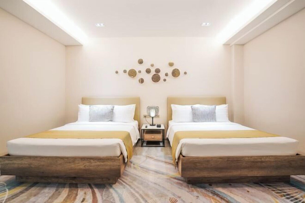 A hotel room with two beds, a nightstand, a wall decoration, and a patterned carpet.