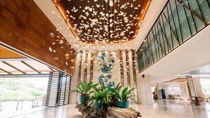 Spaziosa hall con soffitto in legno, ampie finestre e piante in vaso.