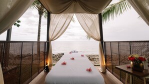 Area benessere sulla spiaggia, con un gazebo bianco, un lettino da massaggio e un tavolino con un vaso di fiori.