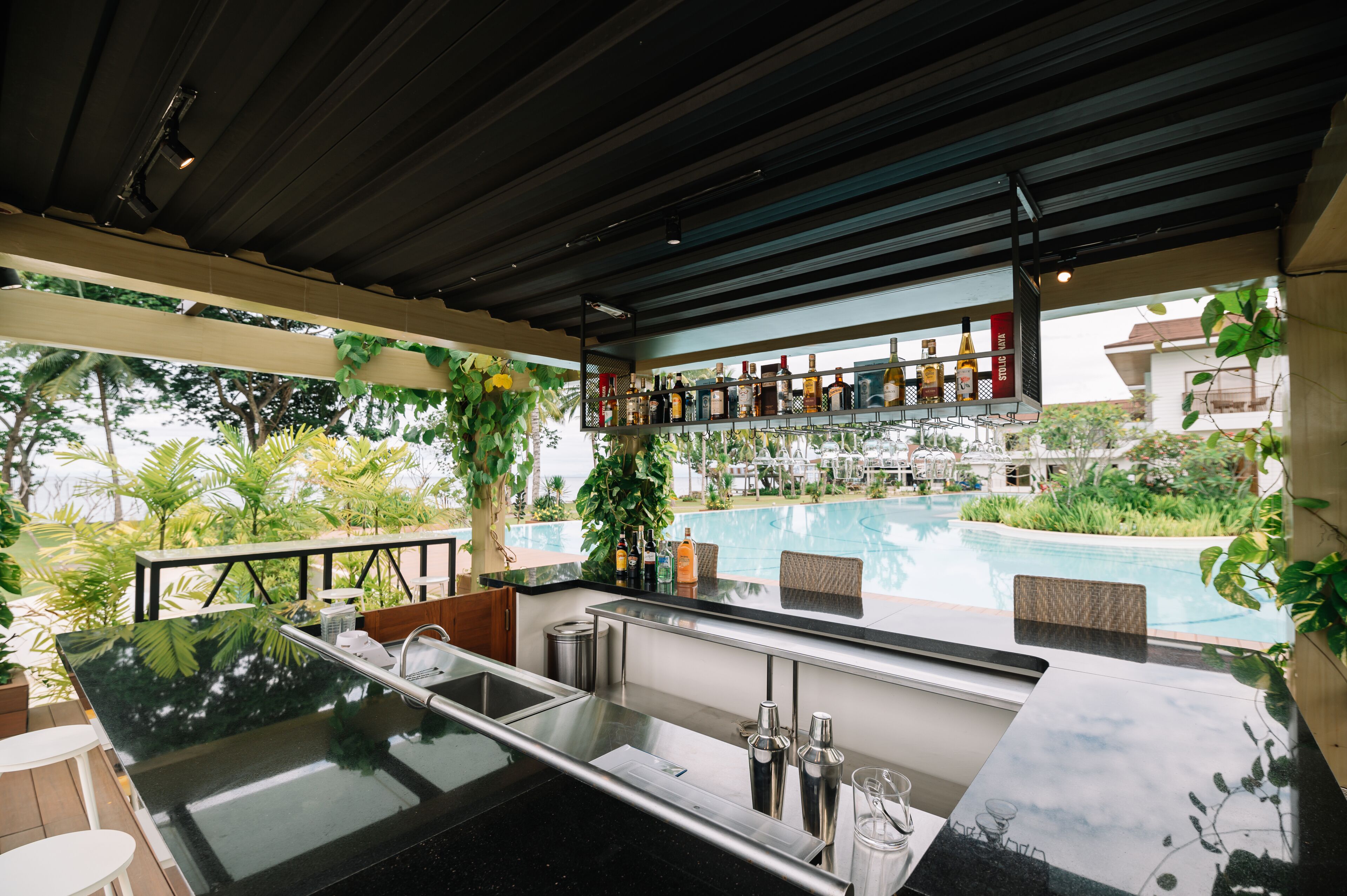 Zona de bar con vista a la piscina, taburetes y una barra con utensilios.