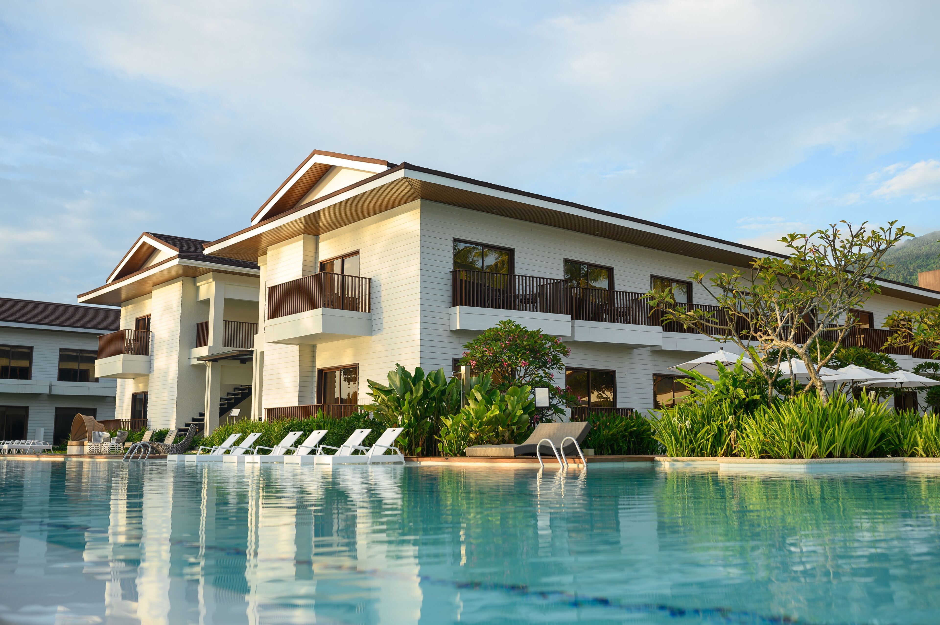 Un hotel moderno con piscina, varios balcones y abundante vegetación.