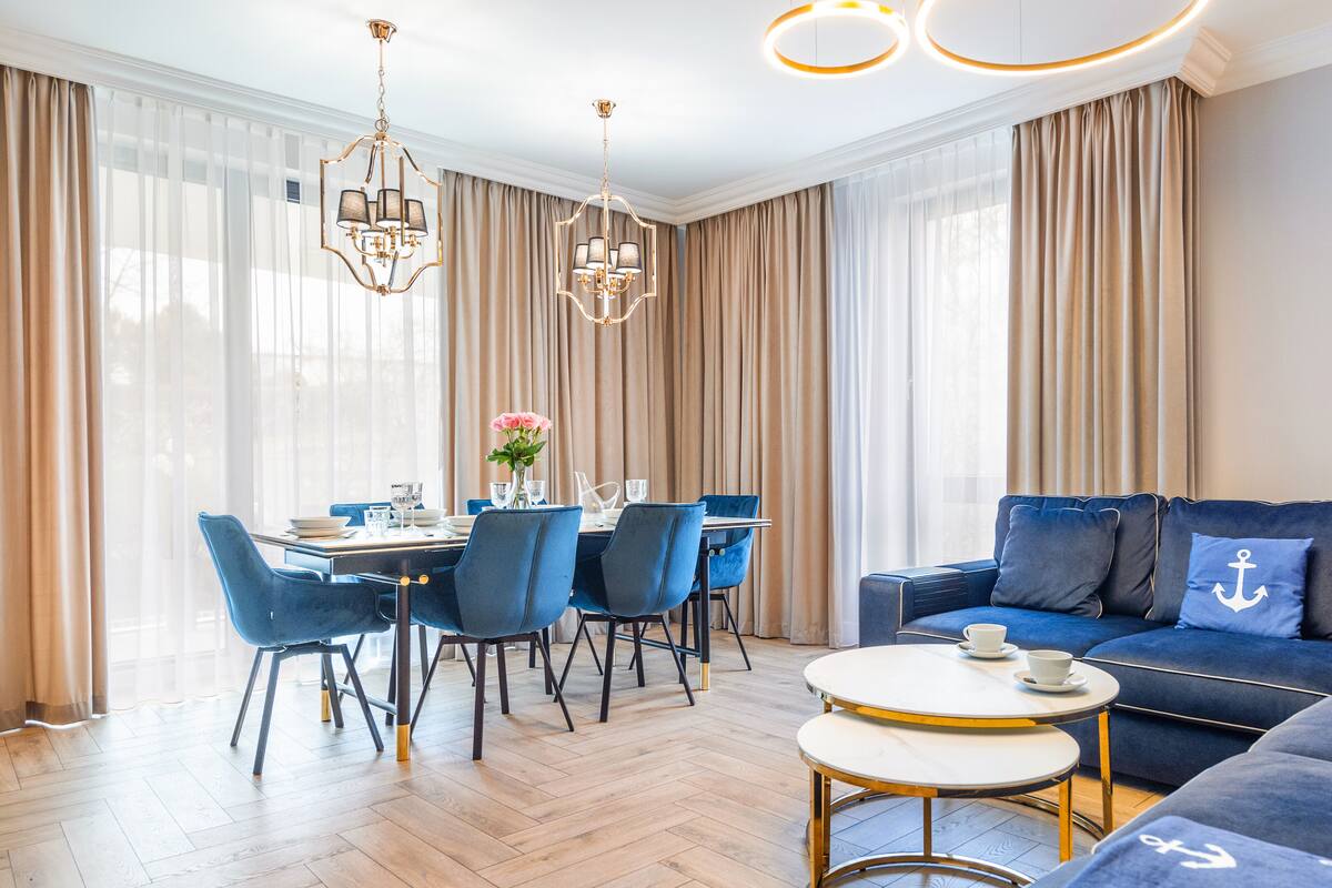 Ein modernes Wohnzimmer mit einem blauen Sofa, einem runden Couchtisch und einem Essbereich mit blauen Stühlen und einem Tisch für zwei Personen.