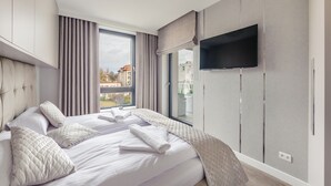 Une chambre d’hôtel moderne dotée d’un grand lit, d’un téléviseur à écran plat fixé au mur et d’une fenêtre donnant sur la ville.