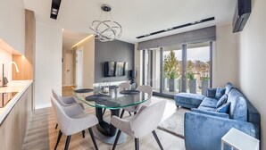 Un salon moderne avec une table à manger en verre, des chaises grises, un canapé bleu et un grand téléviseur fixé au mur.