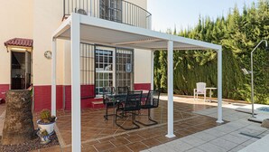 Une terrasse couverte avec une table et des chaises, une plante en pot et une clôture blanche.