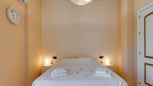 Une chambre d’hôtel comprenant un lit, deux tables de chevet, une horloge murale, un appareil de climatisation et une porte.