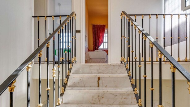 Un escalier en marbre, agrémenté de rampes noires et dorées, mène à une chambre à coucher où se trouvent un lit et des rideaux rouges.