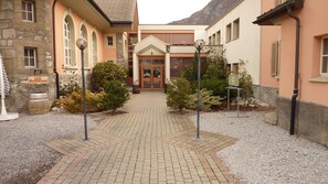 A courtyard with a café sign, stone buildings, and a paved walkway. - Hotel les Berges (Chippis)