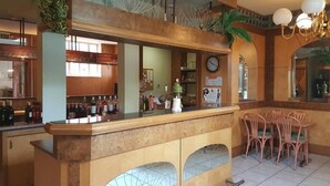 Un espace bar comprenant un comptoir, des étagères remplies de bouteilles, une horloge et un coin salon avec des chaises.