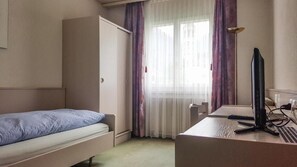 A small, single-room hotel room with a bed, a desk with a computer, and a window with sheer curtains. - Hotel les Berges (Chippis)