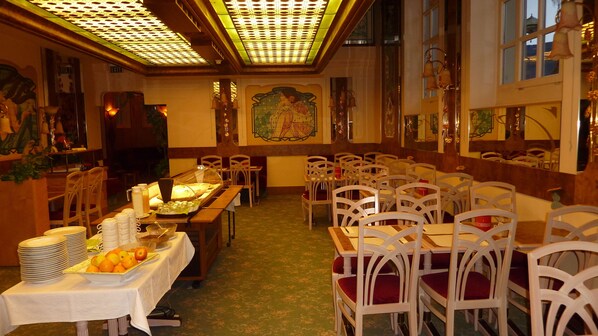 A dining area with tables and chairs, a buffet with food items, and a mural on the wall. - Hotel les Berges (Chippis)