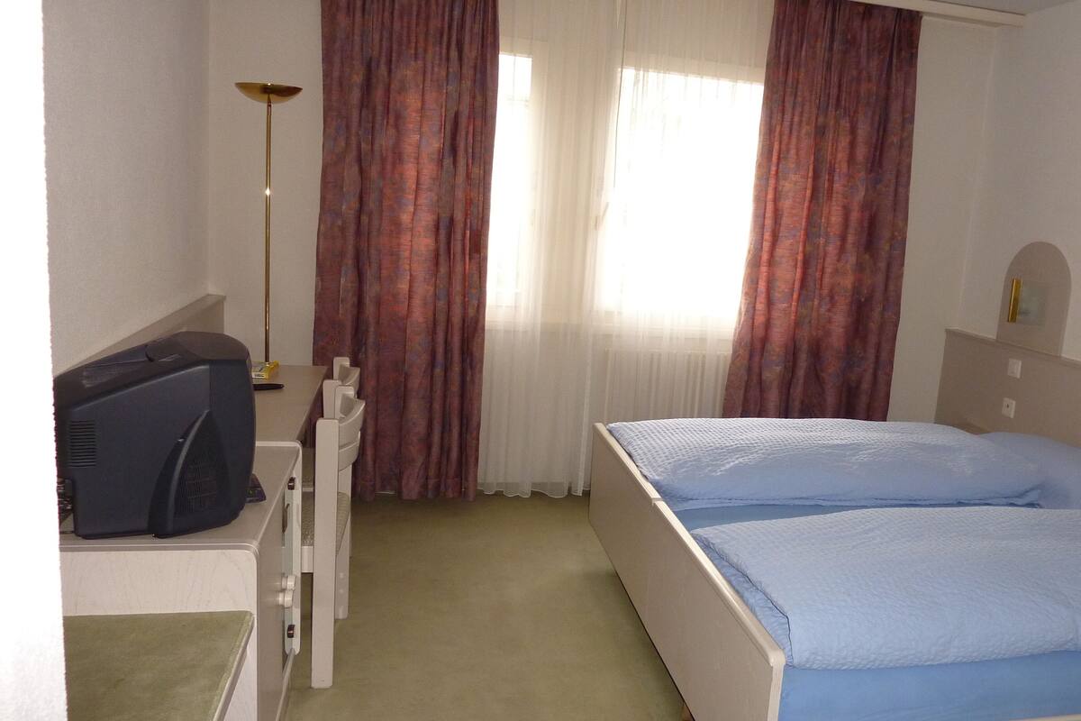 Ein Hotelzimmer mit Bett, Schreibtisch und Fernseher sowie einer Lampe.