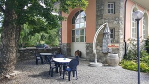 Un espace extérieur aménagé avec des tables et des chaises, un bâtiment en pierre avec une enseigne indiquant la présence d’un café, et un arbre.