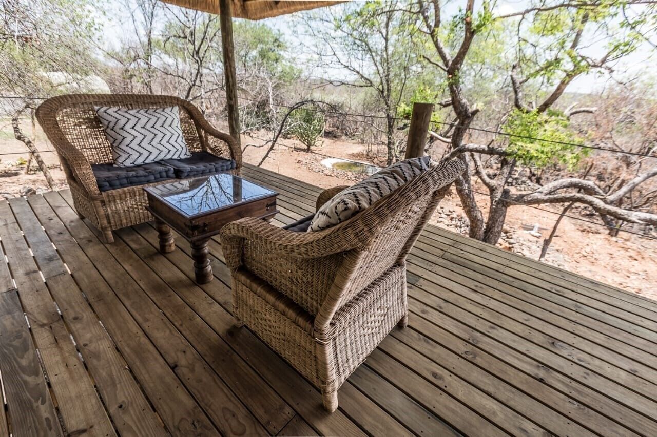 Una terraza de madera con mobiliario de mimbre, incluyendo un sofá y sillones, y una mesita.