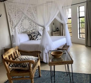 A bedroom with a bed under a white canopy, a wooden chair, a glass table with a bowl, and a patterned rug. - The Wild Blue Lodge SAFARI & SPA (Hoedspruit)